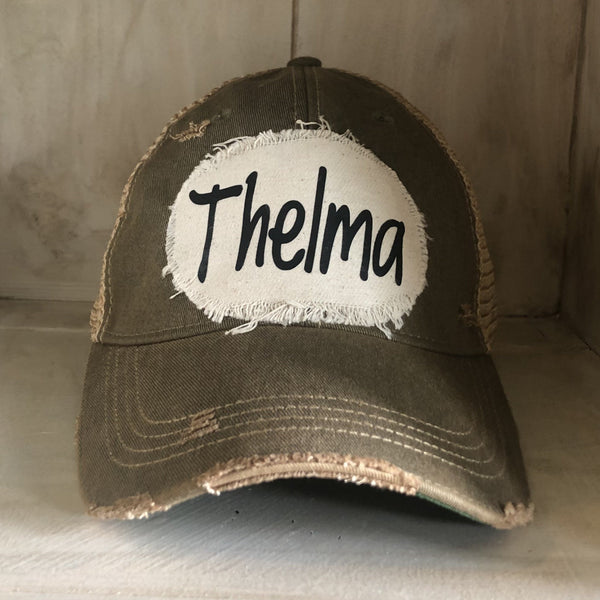 Thelma hat by BohoGroove with black Thelma lettering on a distressed off-white patch on an olive vintage distressed snapback trucker hat.
