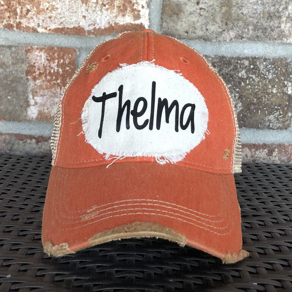 Thelma hat by BohoGroove with black Thelma lettering on a distressed off-white patch on an orange vintage distressed snapback trucker hat.