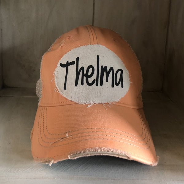 Thelma hat by BohoGroove with black Thelma lettering on a distressed off-white patch on a sherbet vintage distressed snapback trucker hat.