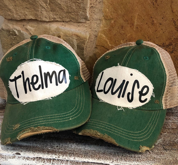 Matching Thelma and Louise hats by BohoGroove with black script lettering on distressed off-white patches on green vintage distressed snapback trucker hats.