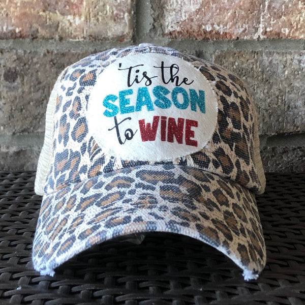 Tis the Season to Wine hat by BohoGroove with black script lettering, blue glitter Season lettering, and red glitter Wine lettering on a distressed off-white custom patch on a leopard vintage distressed snapback.