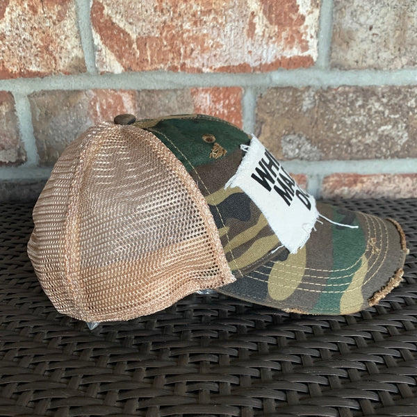 Left side view of a camo vintage distressed snapback trucker hat by BohoGroove featuring a distressed off-white patch with black Whiskey Made Me Do It lettering.